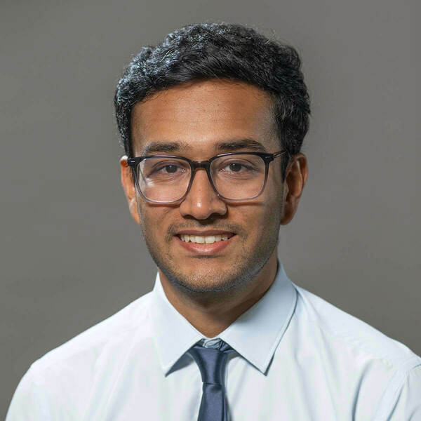 Headshot of Subhasish Mukherjee, a young man wearing glasses, a light blue shirt, and a dark blue tie, smiling against a gray background.