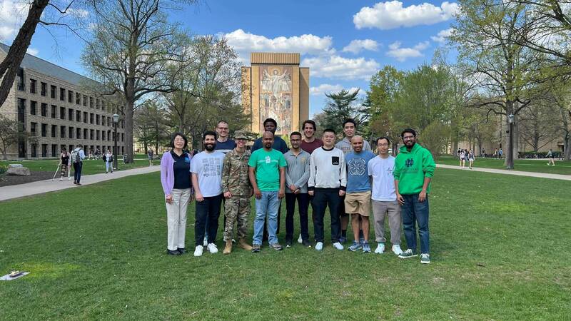 Codesign Lab group photo - eleven people stand on the lawn in front of Hesburgh Library at the University of Notre Dame.  The library's iconic "Touchdown Jesus" mural is visible behind the group.  Spring foliage is visible on the surrounding trees.